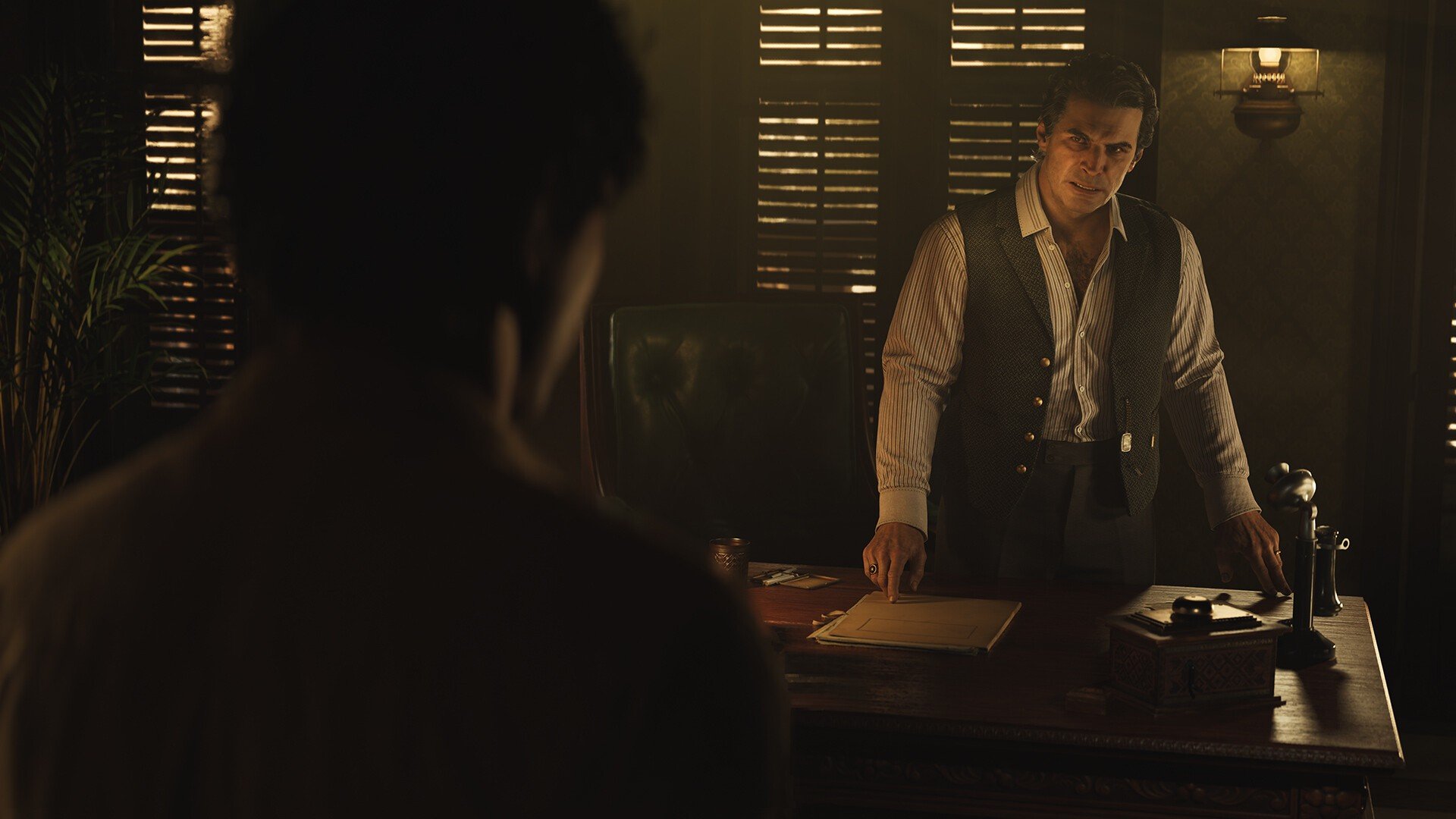 A man who exudes power stands behind an elegant wooden desk with an old-timey phone on it looking stern in a screenshot from Mafia: The Old Country.